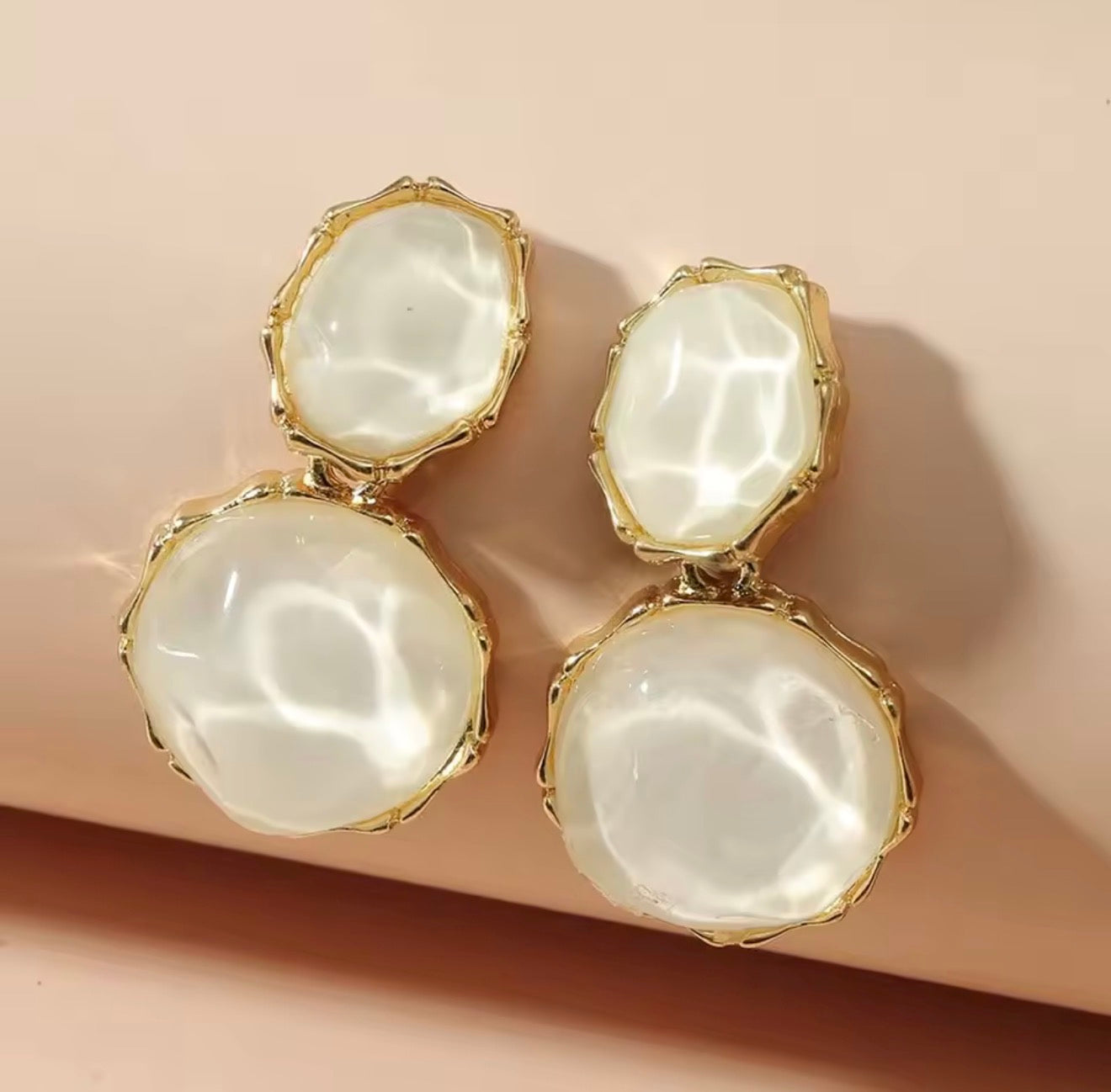 Pair of gold-framed earrings with large white stones on a beige background